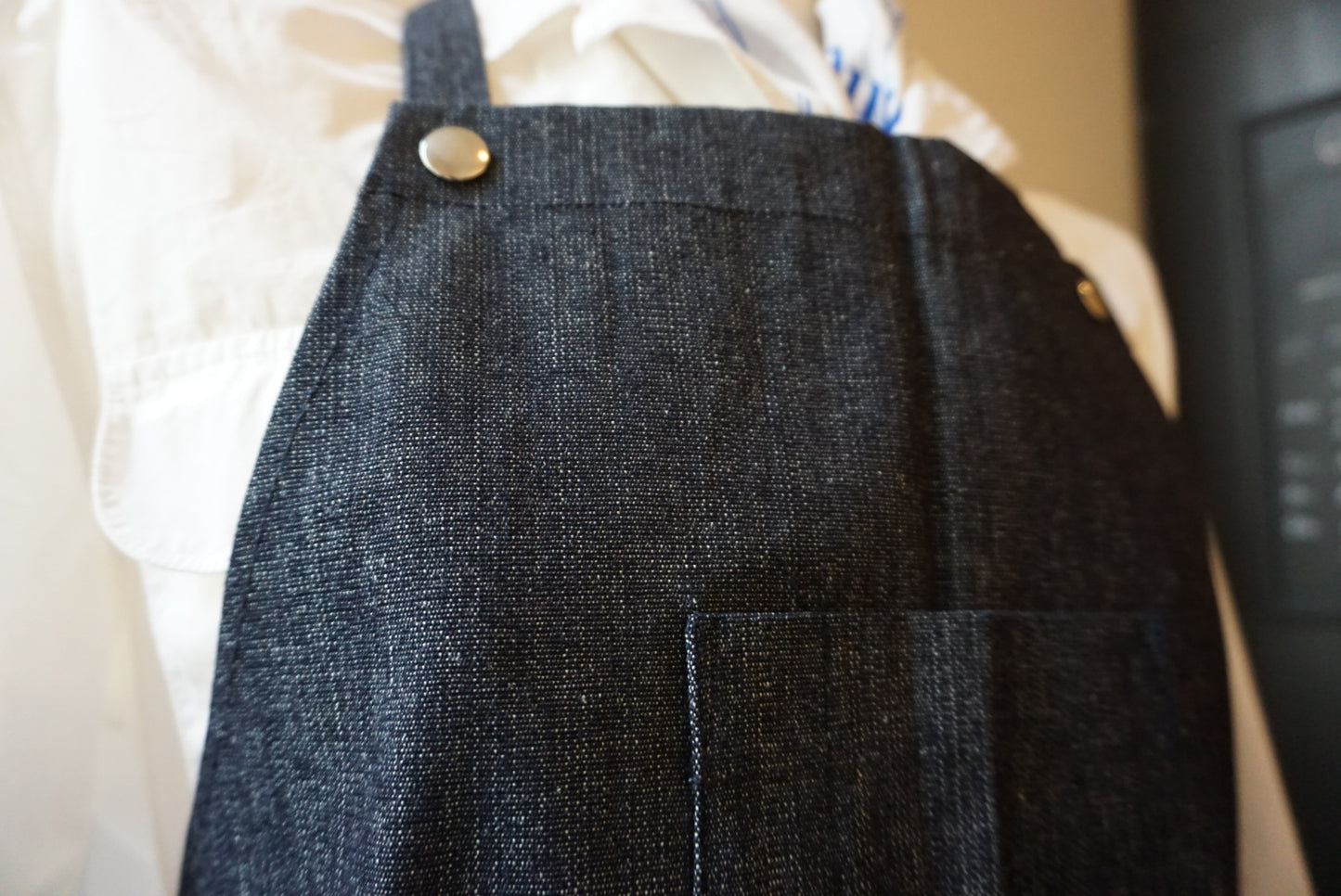 Dark denim apron with a button on a mannequin against a neutral background (TANN Schürze).