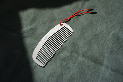 Titanium comb with red string on a textured green surface