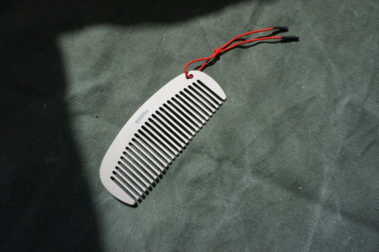 TANN Titanium comb with red string on a textured green surface