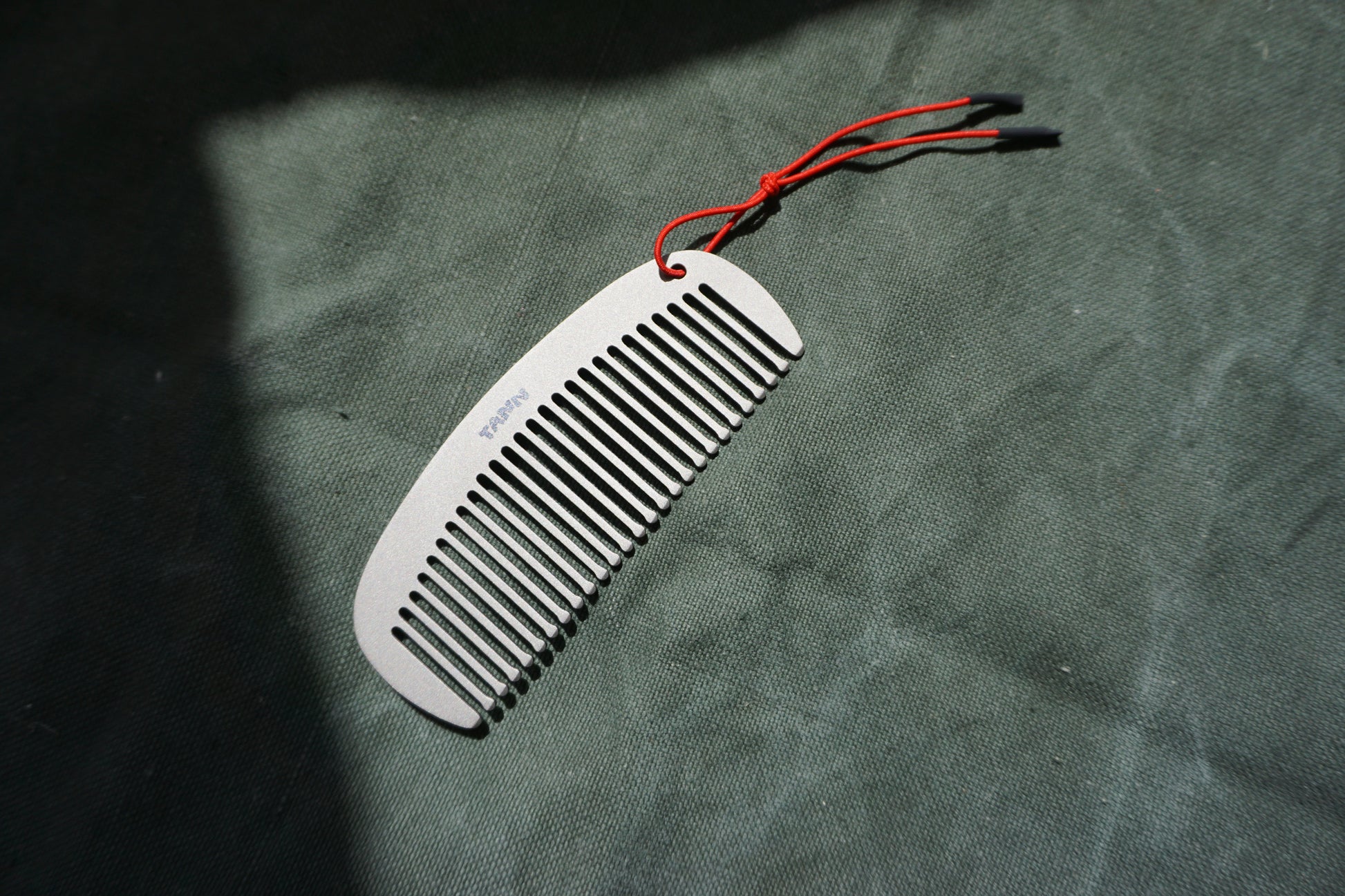 TANN Titanium comb with red string on a textured green surface