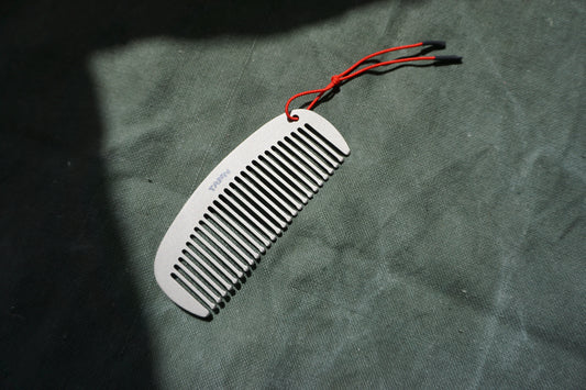 TANN Titanium comb with red string on a textured green surface